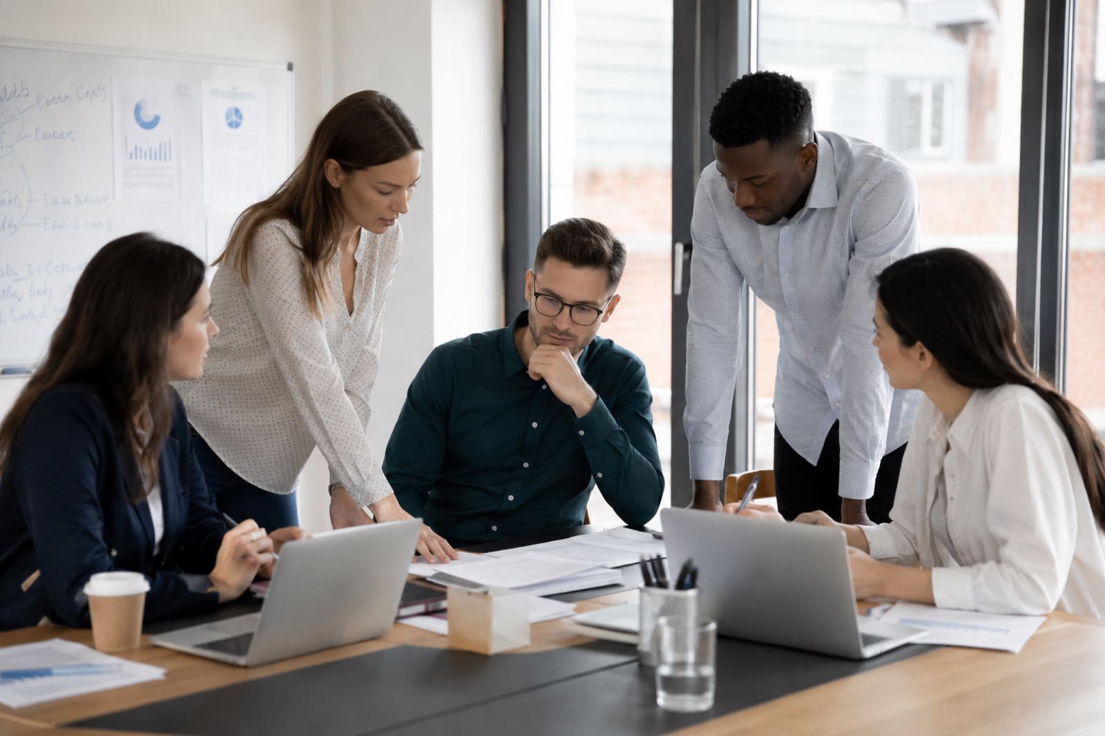 A team leaning in over a table together, working through something on a laptop